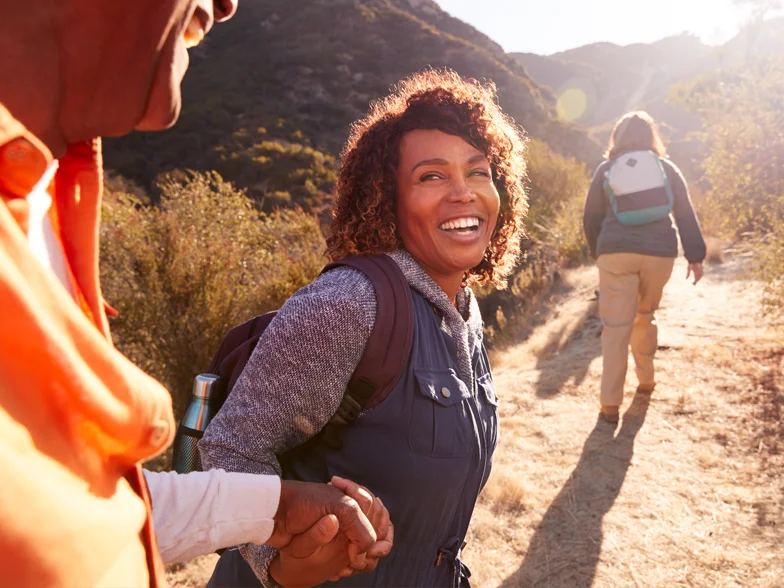 A smiling woman helping an older man on a trail in the countryside.